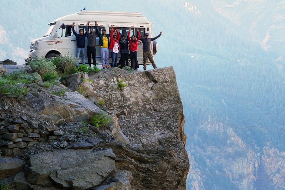 A group of friends celebrating on a cliff edge with a van in the background during a mountain adventure.